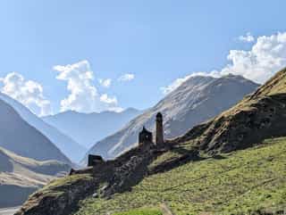 An abandoned tower on a hill in the Georgian mountains under a clear blue sky.