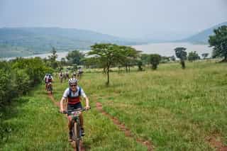 Veloglobe deelnemers fietsen langs een rivier in Rwanda, met de weelderige, tropische omgeving op de achtergrond.