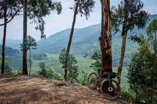 Fiets van een Veloglobe-deelnemer leunt tegen een boom in Rwanda, omgeven door weelderige groene heuvels en een adembenemend landschap op de achtergrond.