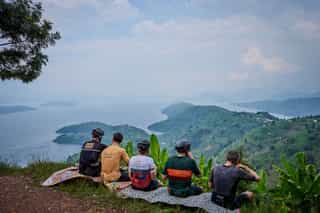 Deelnemers van Veloglobe die zittend aan het eten zijn met een prachtig uitzicht over het Kivu meer.