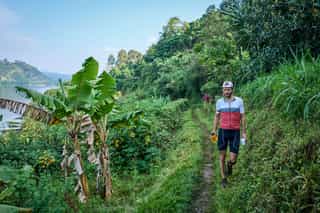 Veloglobe deelnemer aan het wandelen in zijn veloglobe outfit op een singletrack tussen de groene Rwandese natuur.